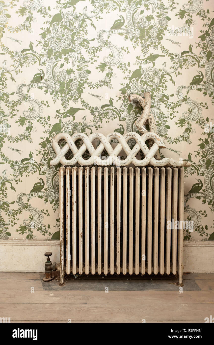 Pezzo di rotte di recupero architettonico sul vecchio radiatore nella hall di entrata con carta da parati Foto Stock