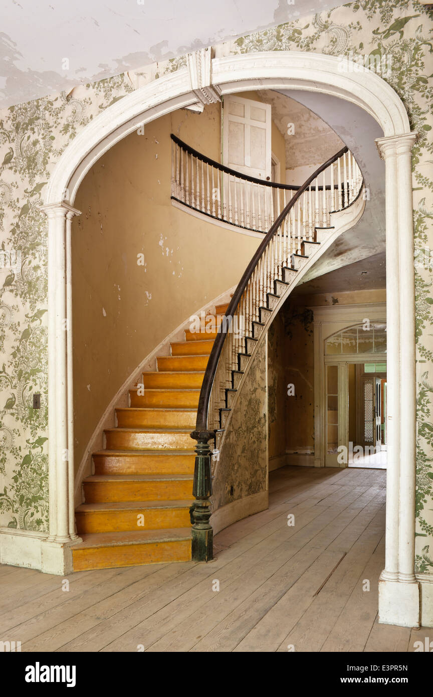 Scala ellittica in corridoio con arch, peeling carta da parati con motivi geometrici e pavimenti in legno Foto Stock