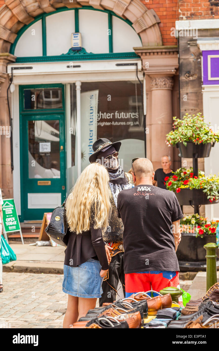 Regno Unito Inghilterra Leek, Staffordshire. Un uomo vestito da cowboy e indossa uno scheletro maschera facciale, parlando agli acquirenti in città mercato Foto Stock