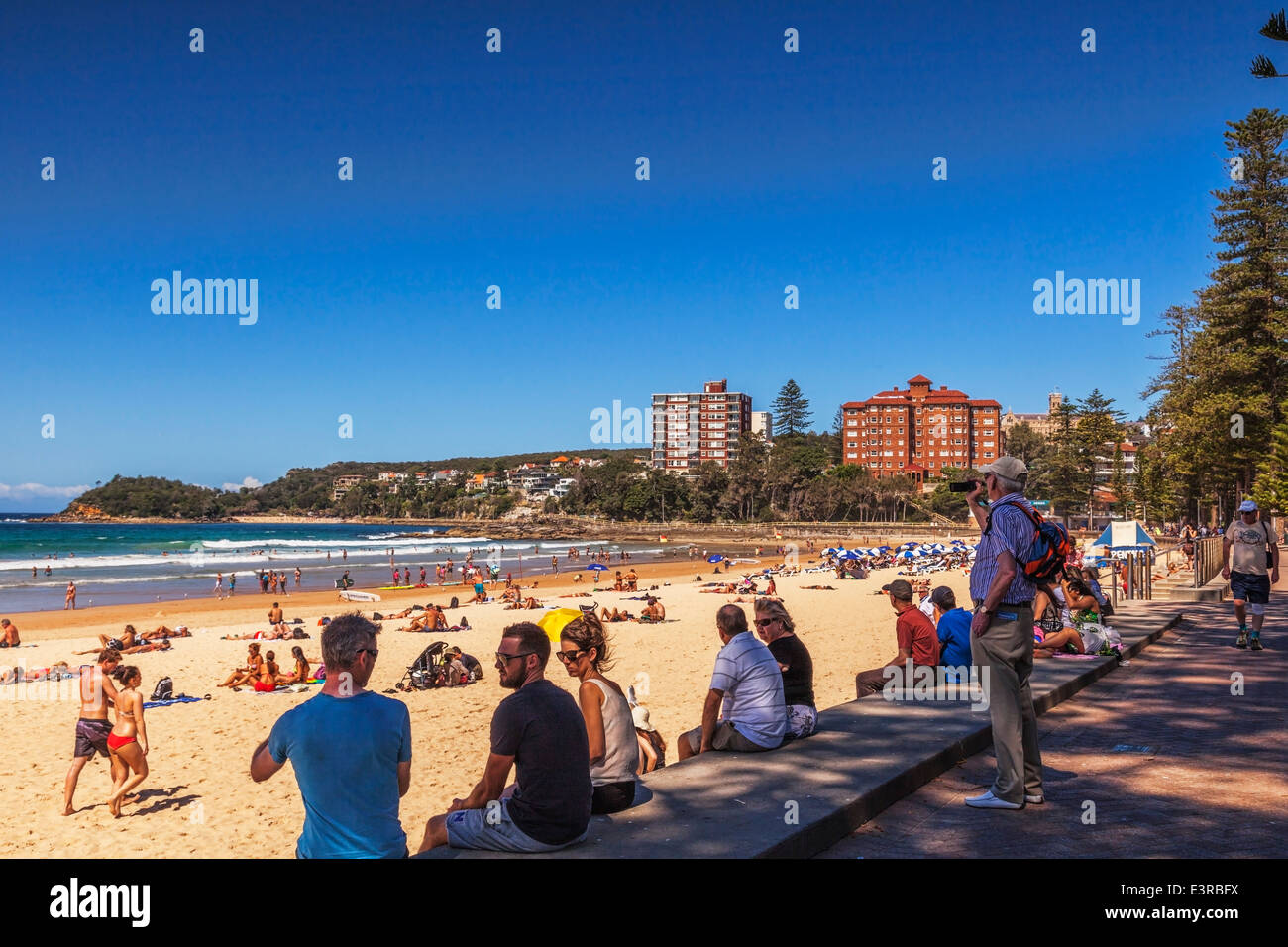 Manly Beach, Sydney, Australia. Senior uomo prendendo foto con il suo telefono cellulare. Linea di persone sedute su una parete. Foto Stock