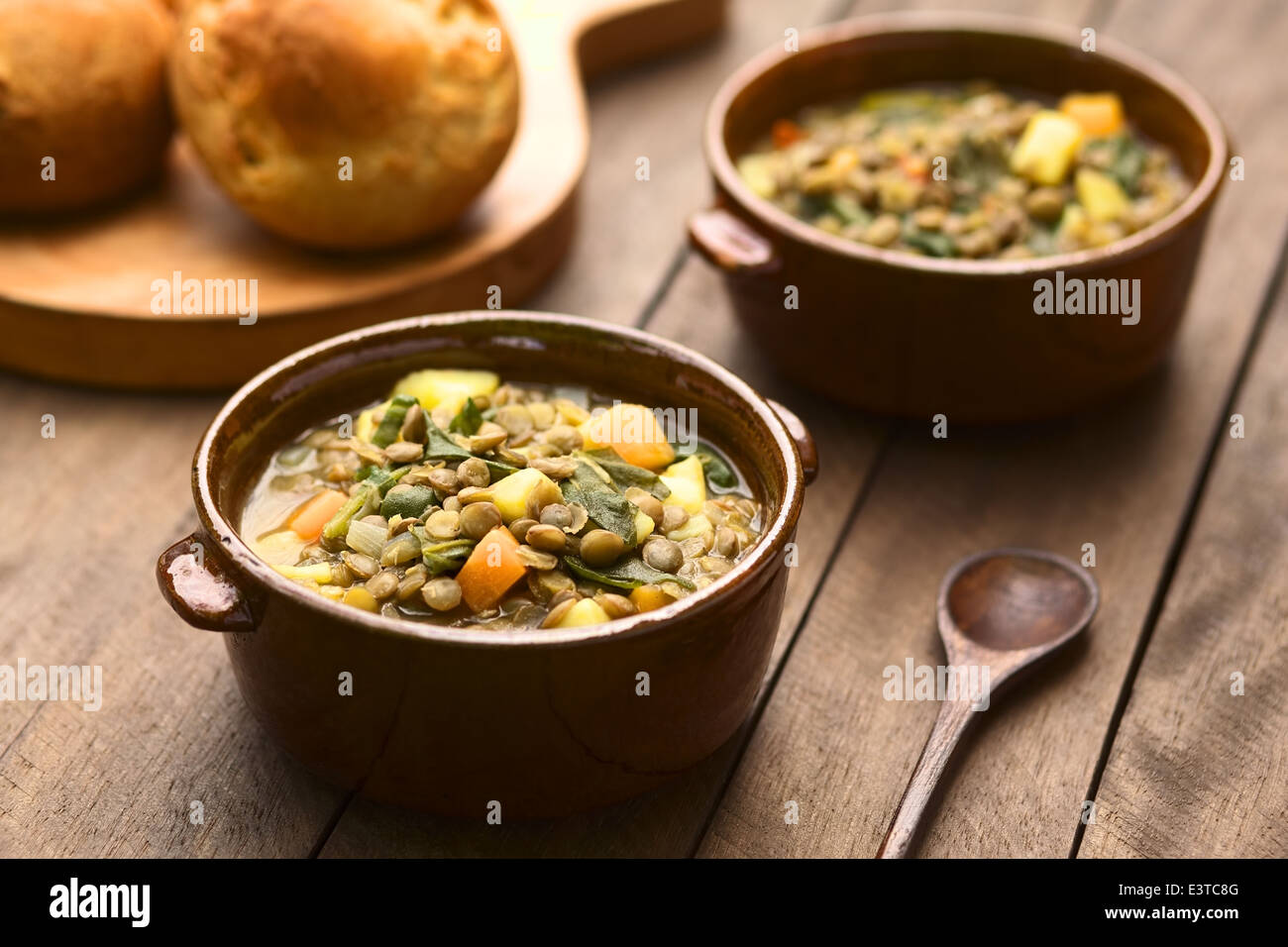 Vegetariano zuppa di lenticchie, spinaci, la patata, la carota e la cipolla è servita in marrone scuro ciotole con ciambelle in retro Foto Stock