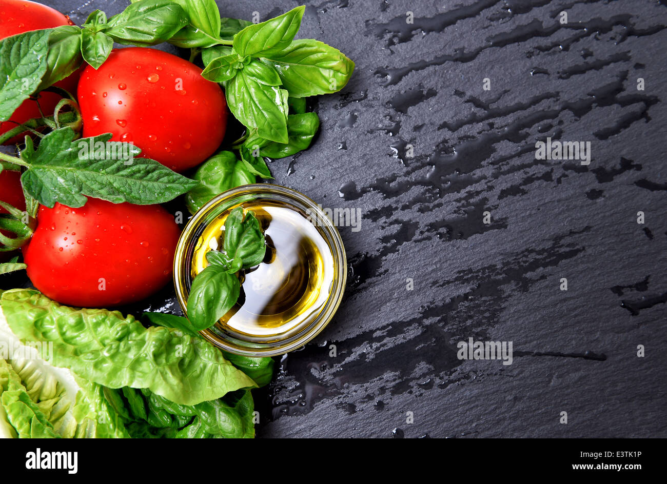 Il basilico fresco erbe e pomodori con olio di oliva su sfondo nero. sani ingredienti alimentari Foto Stock