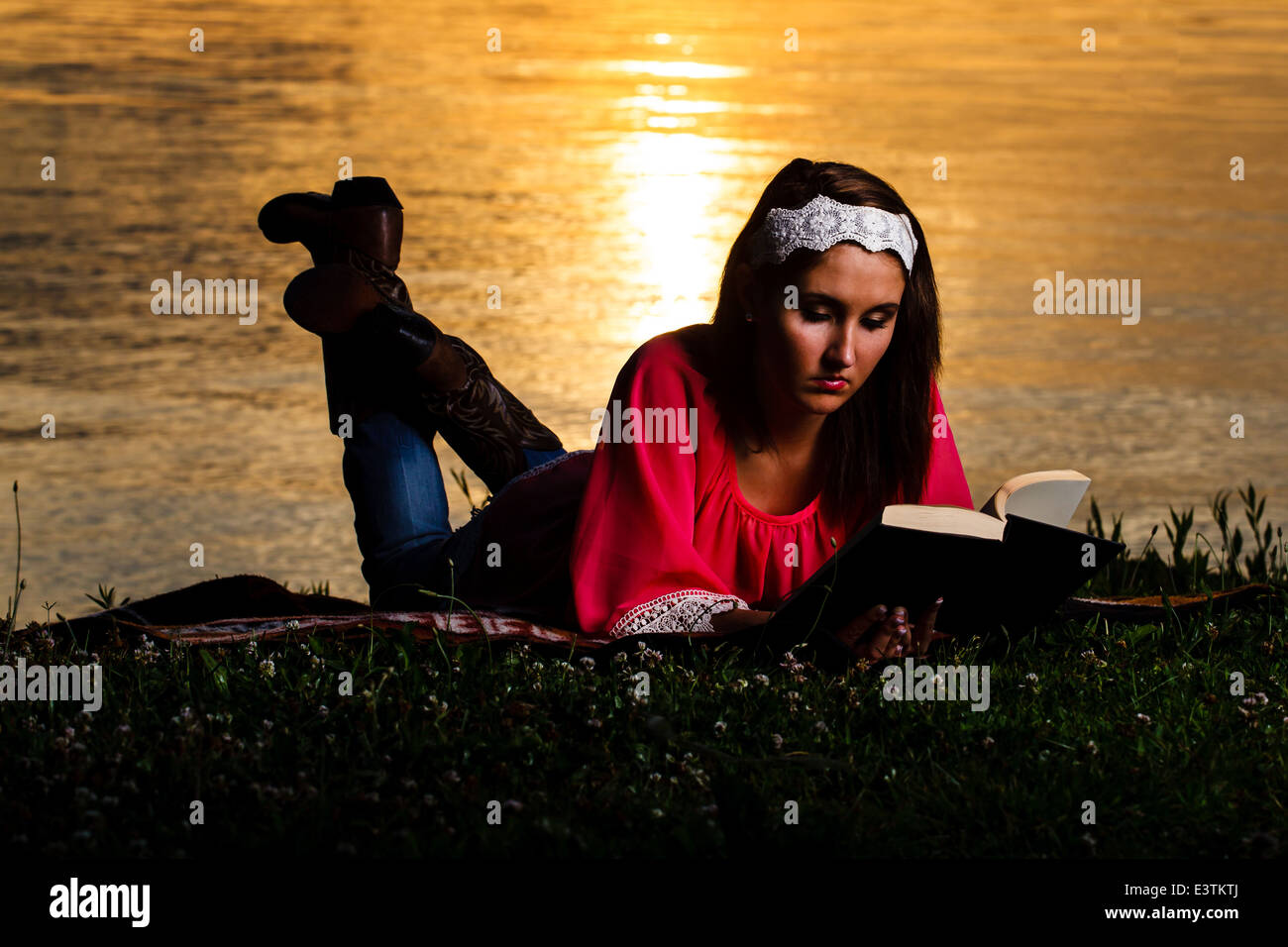 Una bella ragazza la lettura di un libro sulle rive del lago del Kentucky come sorge il sole. Foto Stock