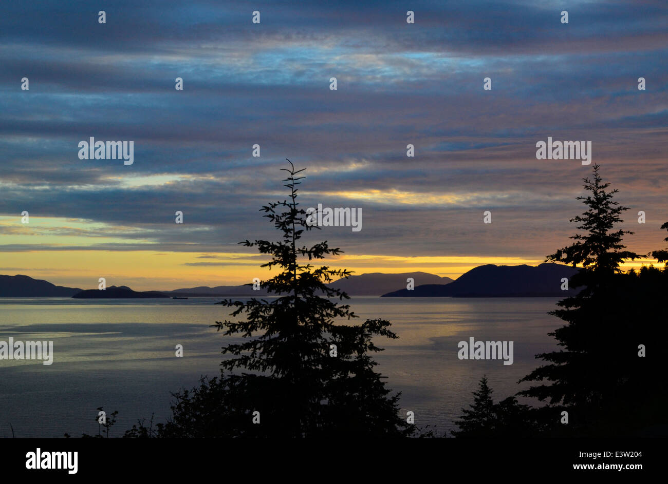 Tramonto sulle acque della baia di Samish, lungo Chuckanut Drive nello Stato di Washington. Gli alberi e le montagne dalle isole locali. Foto Stock