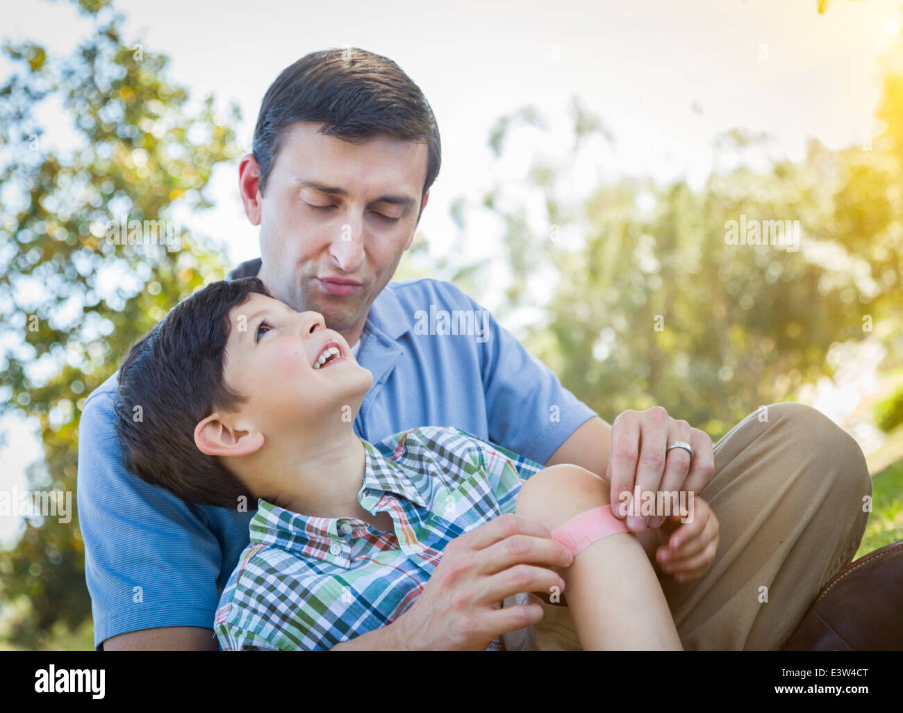 Padre amorevole mette un cerotto sul ginocchio del suo giovane figlio nel parco. Foto Stock