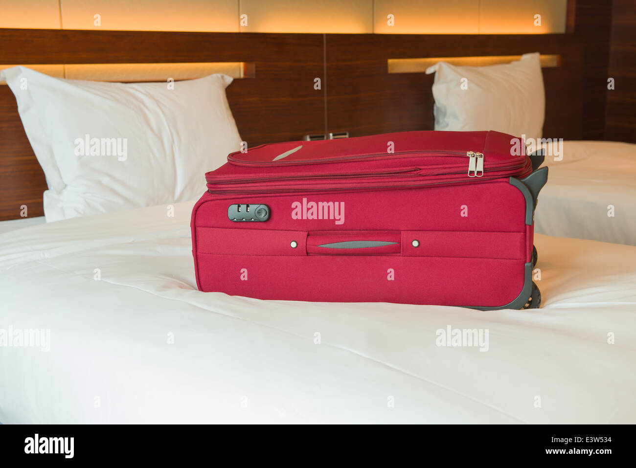 Red valigia sul letto in una stanza di un hotel Foto Stock