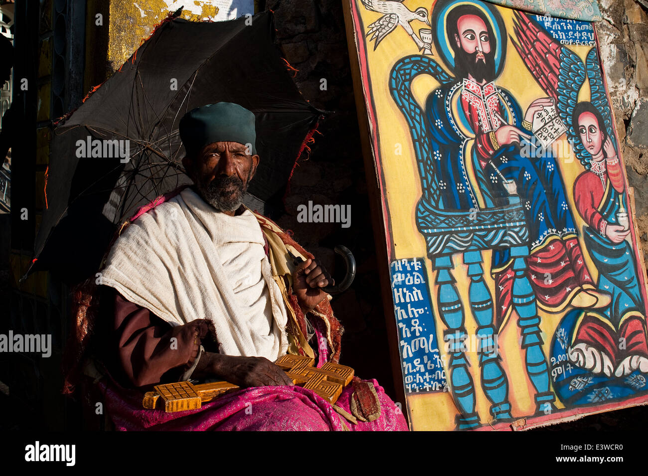 Sacerdote ortodosso raccogliere denaro in prossimità di un dipinto di un santo etiope ( cioè saint Mikael) ( Etiopia) Foto Stock