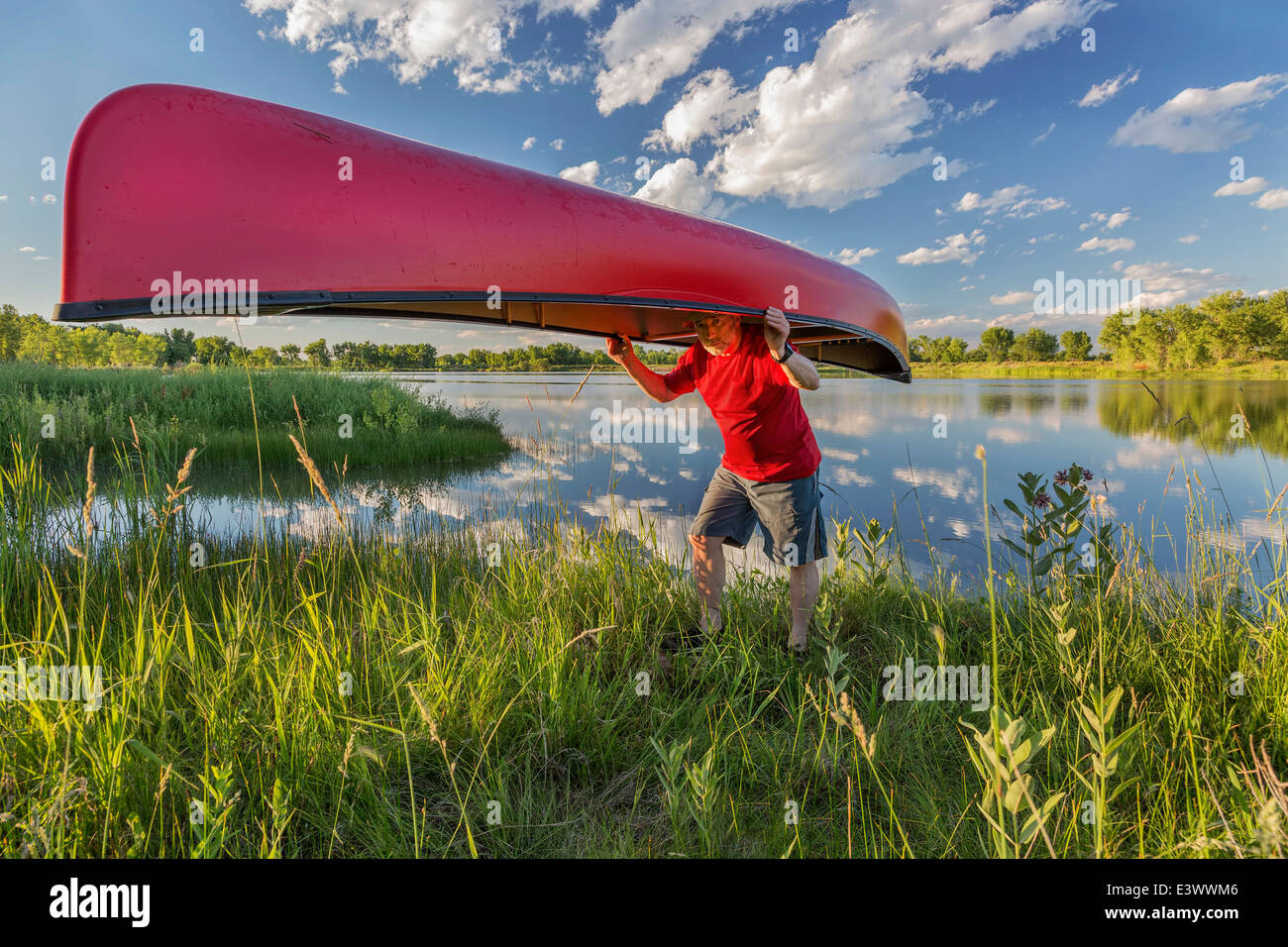 Senior paddler maschio portaging un rosso canoa sulla riva del lago Foto Stock