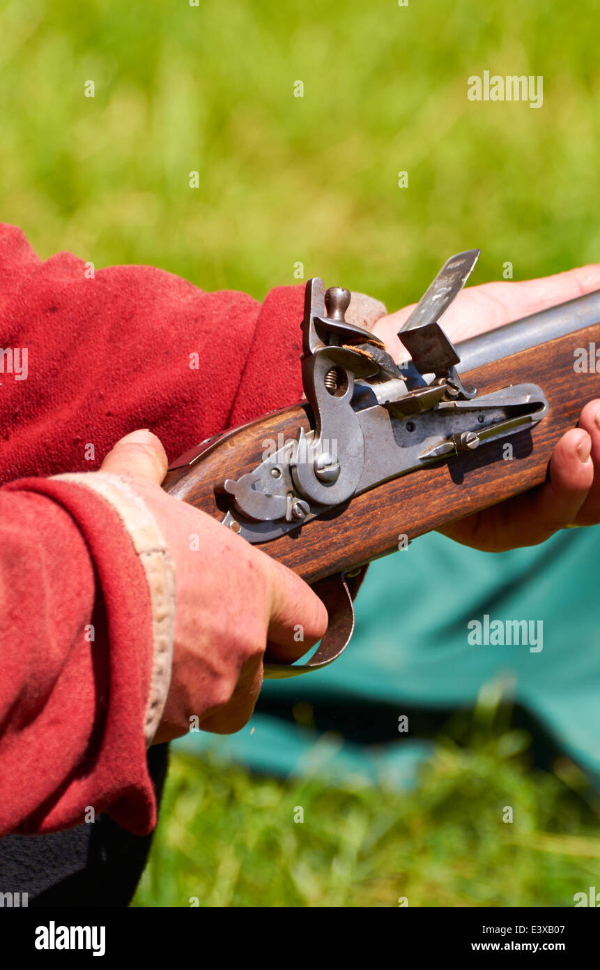 Attore in British Redcoat uniforme tenendo un 'Brown Bess' flintlock moschetto mostrante il dettaglio della pietra focaia e la polvere del meccanismo pan. Foto Stock