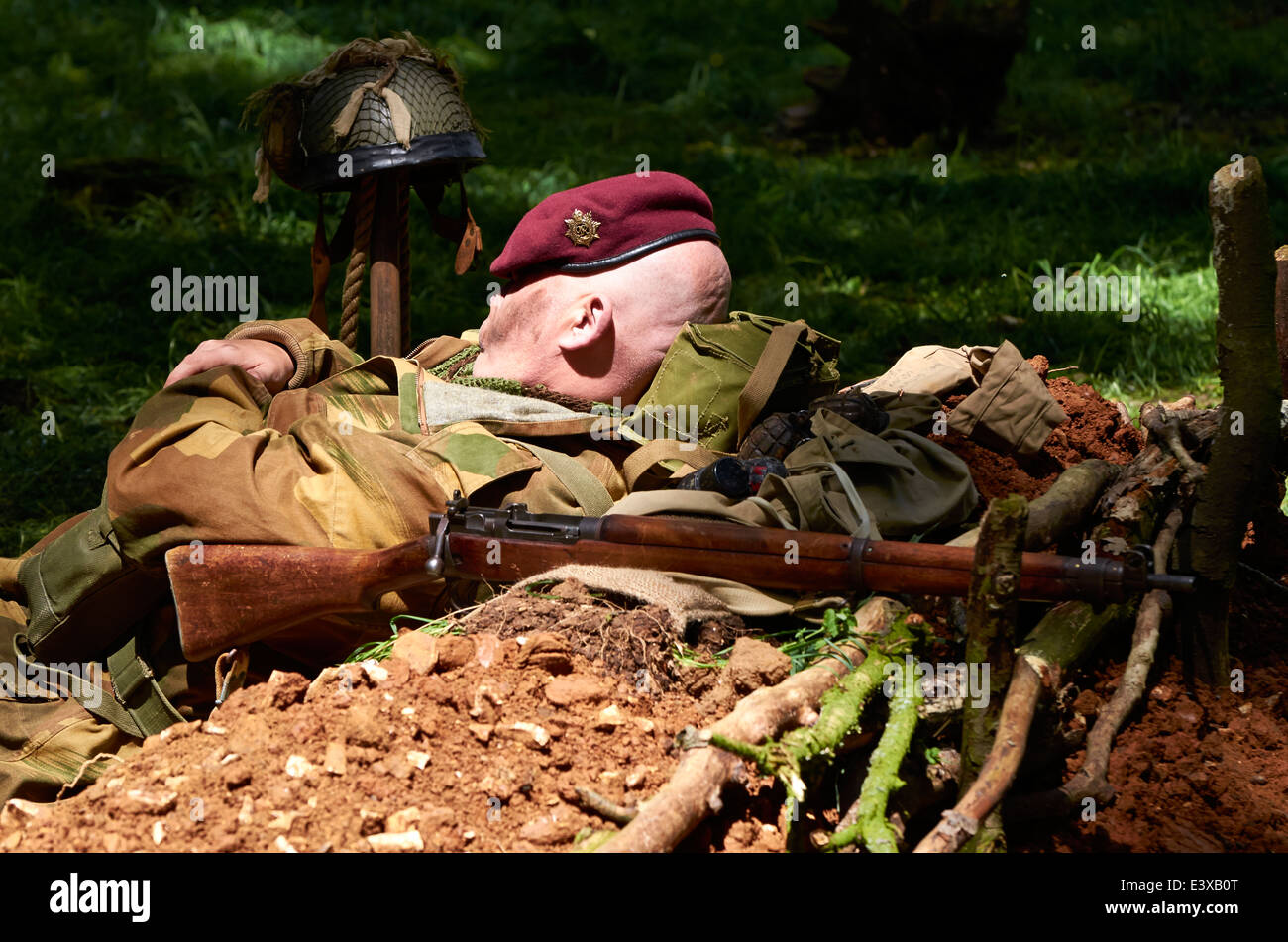 In appoggio prima della battaglia. Militari di ri-enactor in WW2 Esercito Britannico paratroop dozes uniforme in un foro di fox, fucile pronto all'uso. Foto Stock