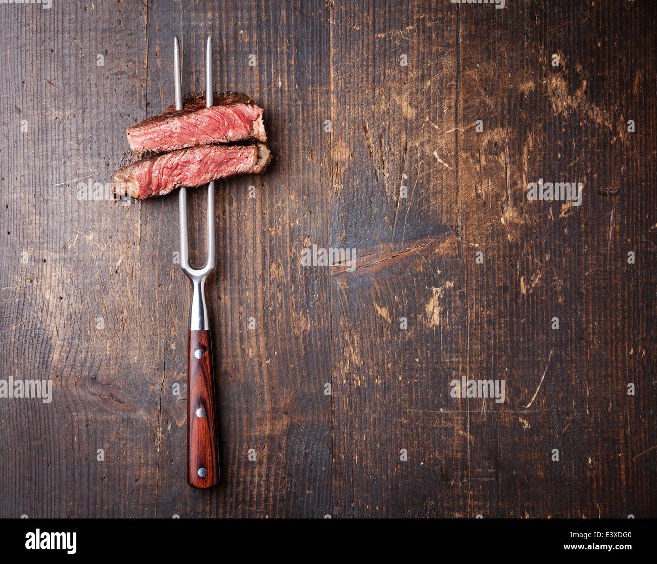 Fette di carne di manzo sulla forcella di carne su scuro dello sfondo in legno Foto Stock