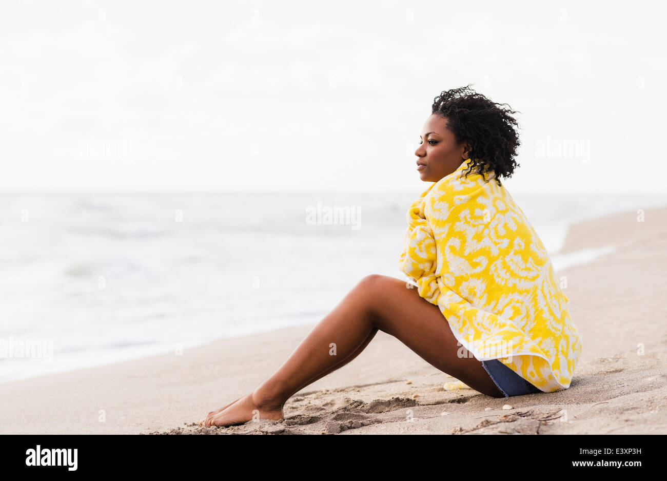 African American donna avvolta in asciugamano sulla spiaggia Foto Stock