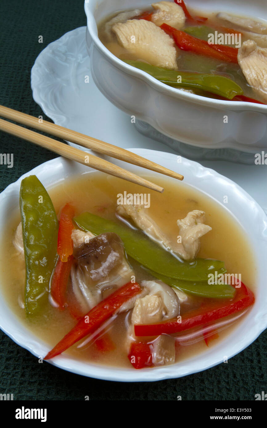 Ciotola e terrina di Asian zuppa di pollo con pepe rosso e piselli della neve sulla biancheria di colore verde con bacchette Foto Stock