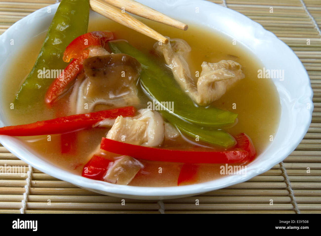 Ciotola di Asian zuppa di pollo con pepe rosso e neve piselli in bianco ciotola sul tappetino di bambù con bacchette Foto Stock