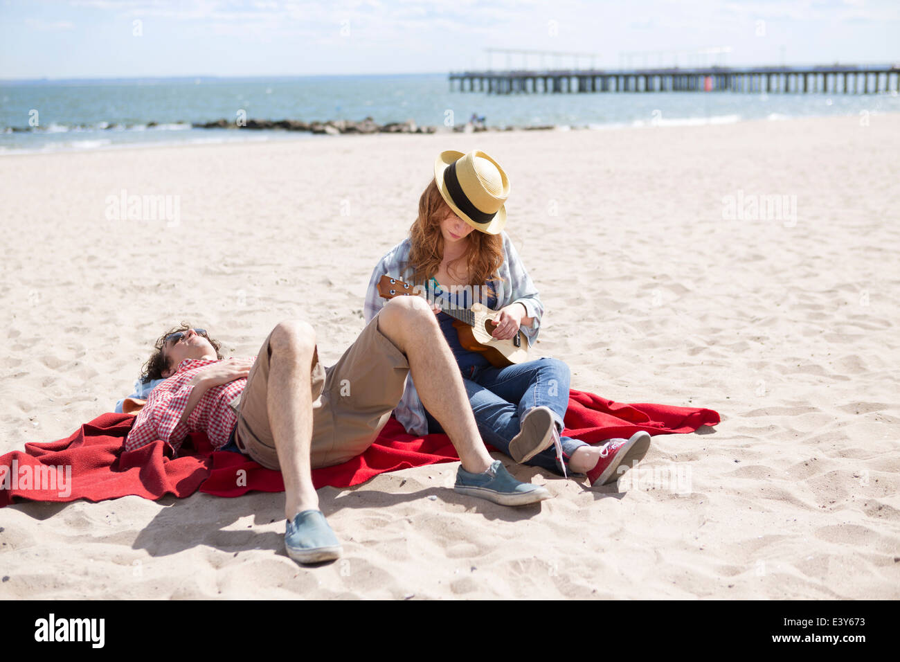 Matura a prendere il sole e giocare ukulele sulla spiaggia Foto Stock