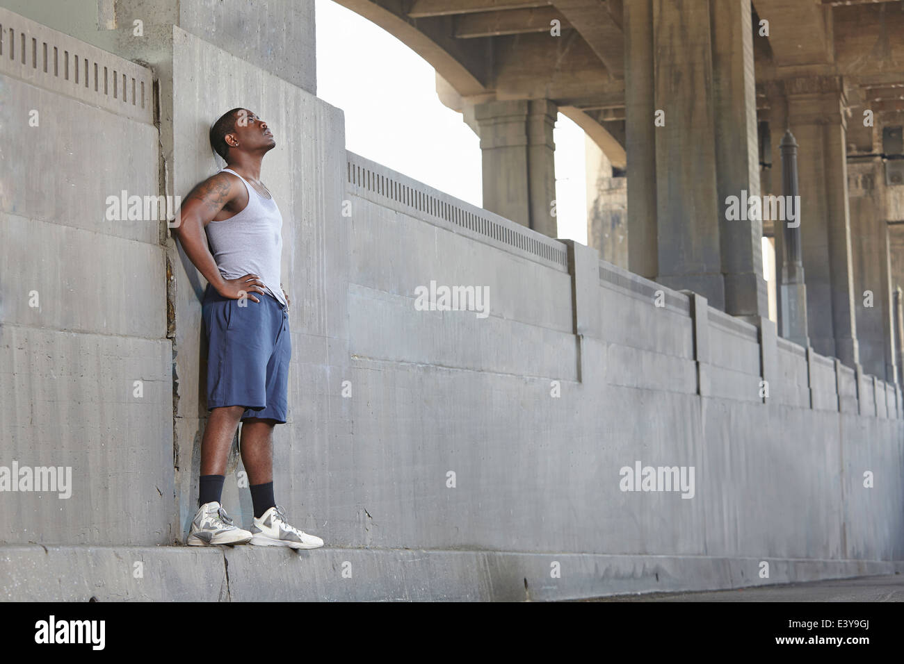 Esaurito giovane maschio runner appoggiata contro il ponte della città Foto Stock