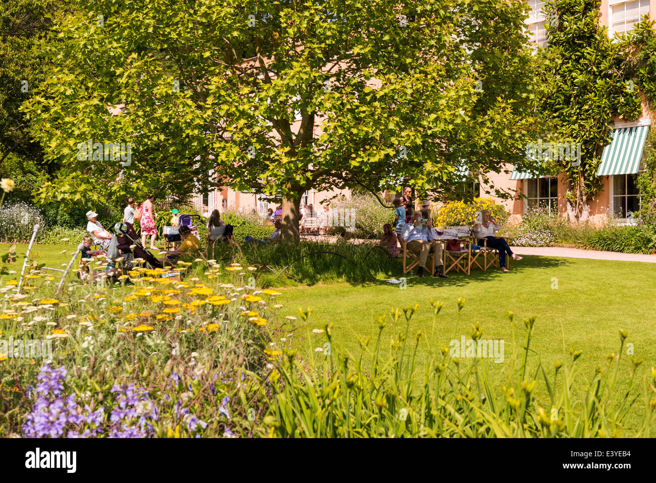 East Devon, in Inghilterra. Un country house garden scena con gente seduta sotto un albero in ombra. Foto Stock