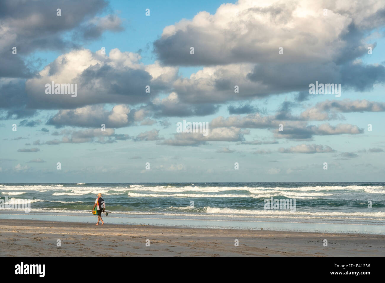 Australia, Nuovo Galles del Sud, Pottsville, il pescatore a piedi lungo la spiaggia con il surf e le nuvole scure Foto Stock