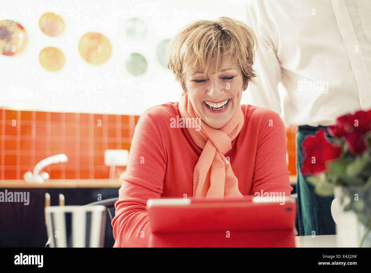 Donna matura con tavoletta digitale in cucina Foto Stock