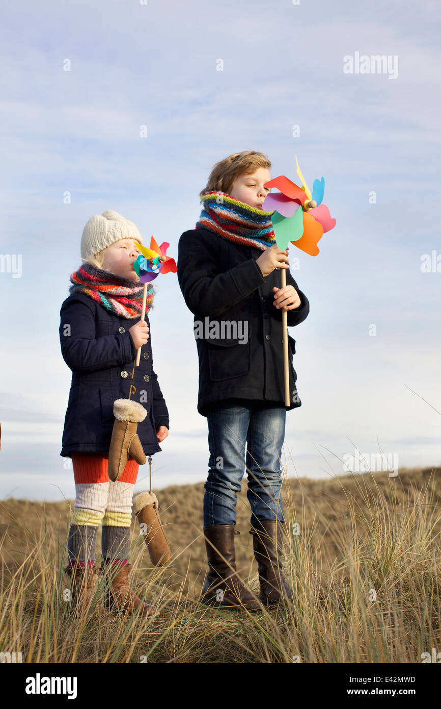 Fratello e Sorella soffiando su carta mulini a vento a costa Foto Stock