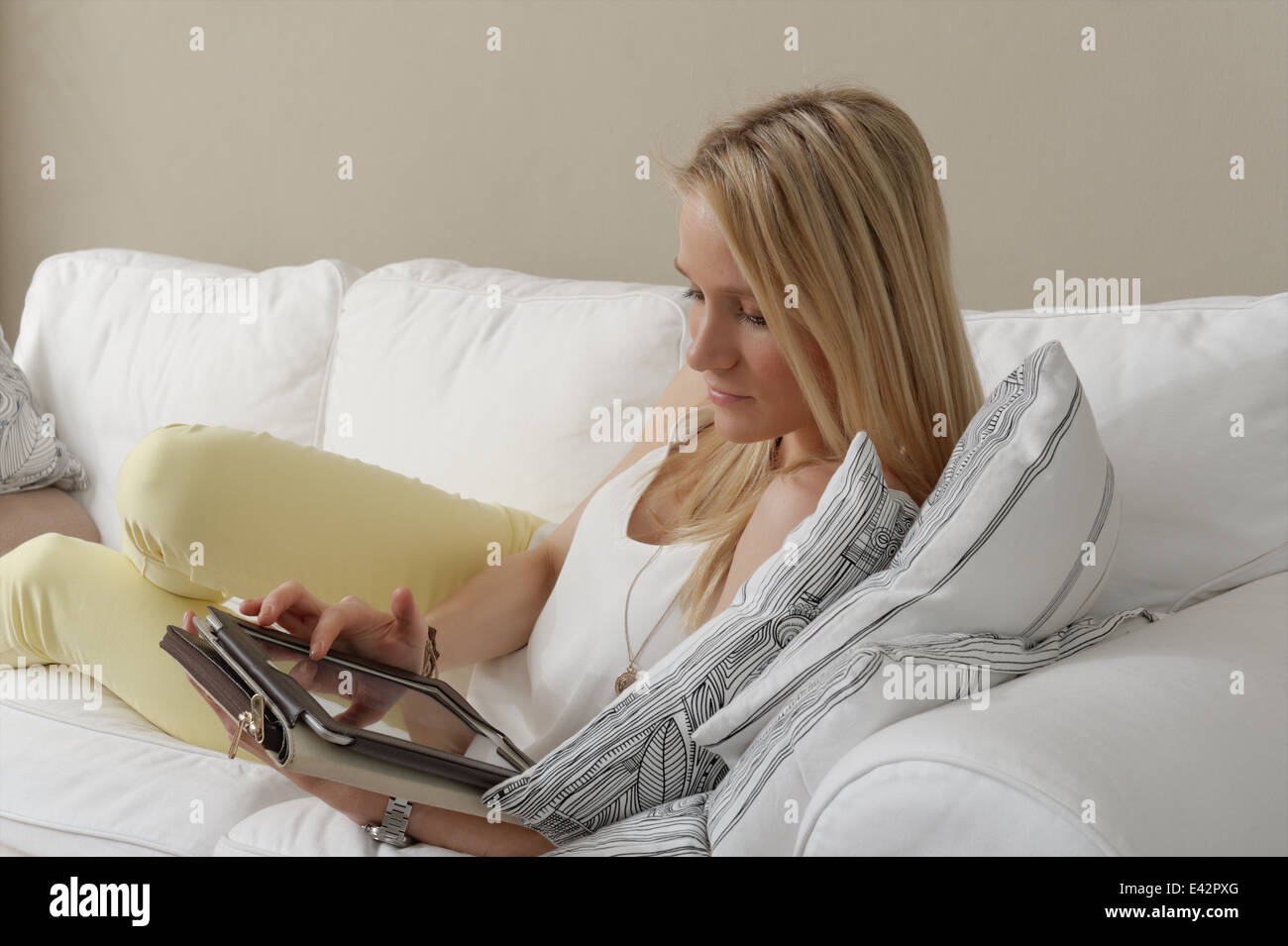 Giovane donna sul divano utilizzando il touchscreen su tavoletta digitale Foto Stock