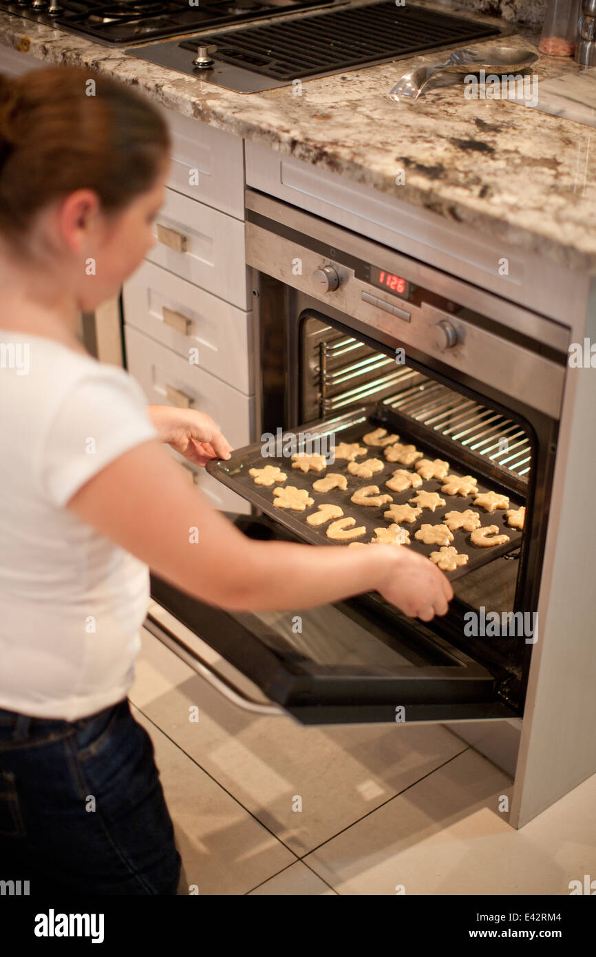Ragazza adolescente ponendo il vassoio di cottura di biscotti in forno Foto Stock
