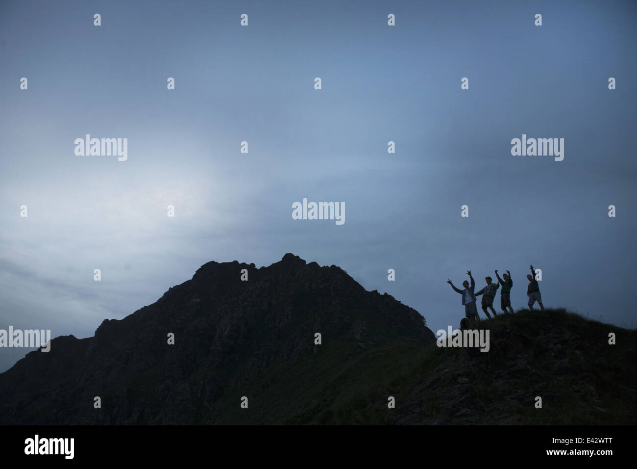 Silhouette di quattro giovani uomini adulti con le braccia sollevate sulla cima della montagna Foto Stock
