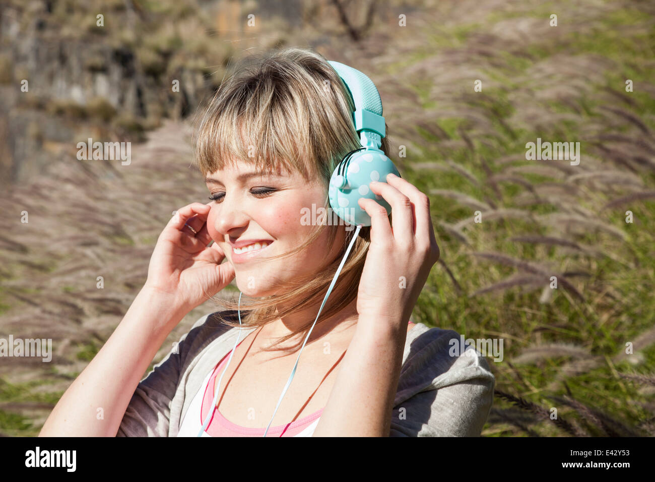 Giovane donna con gli occhi chiusi ascoltando le cuffie in erba lunga Foto Stock