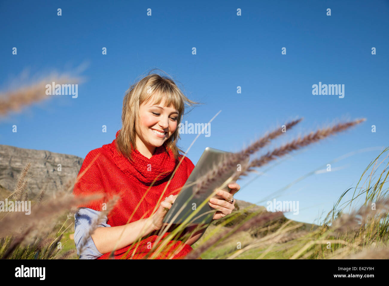 Giovane donna seduta in erba lunga utilizzando touch screen sulla tavoletta digitale Foto Stock