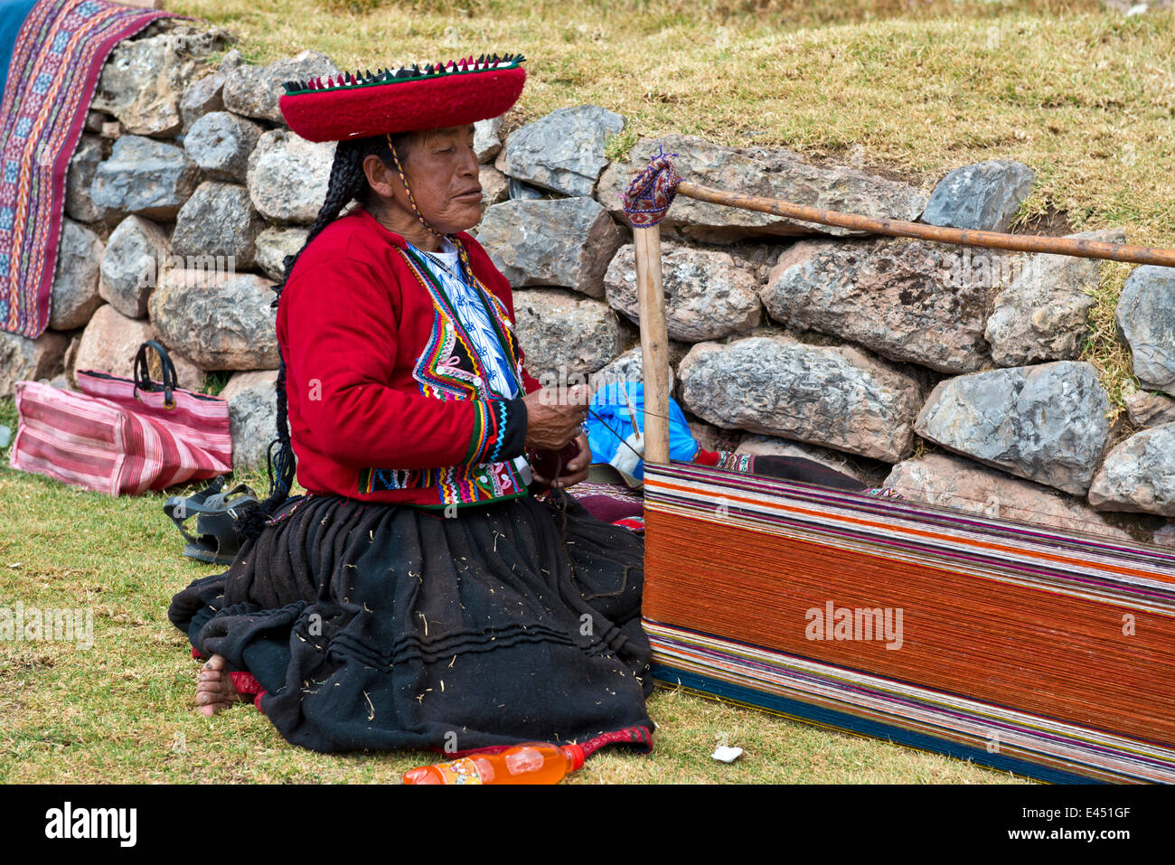 Donna anziana che indossa un cappello, Indiani Quechua in un abito tradizionale, seduto sul pavimento e lavorando su una barella di un telaio di tessitura Foto Stock
