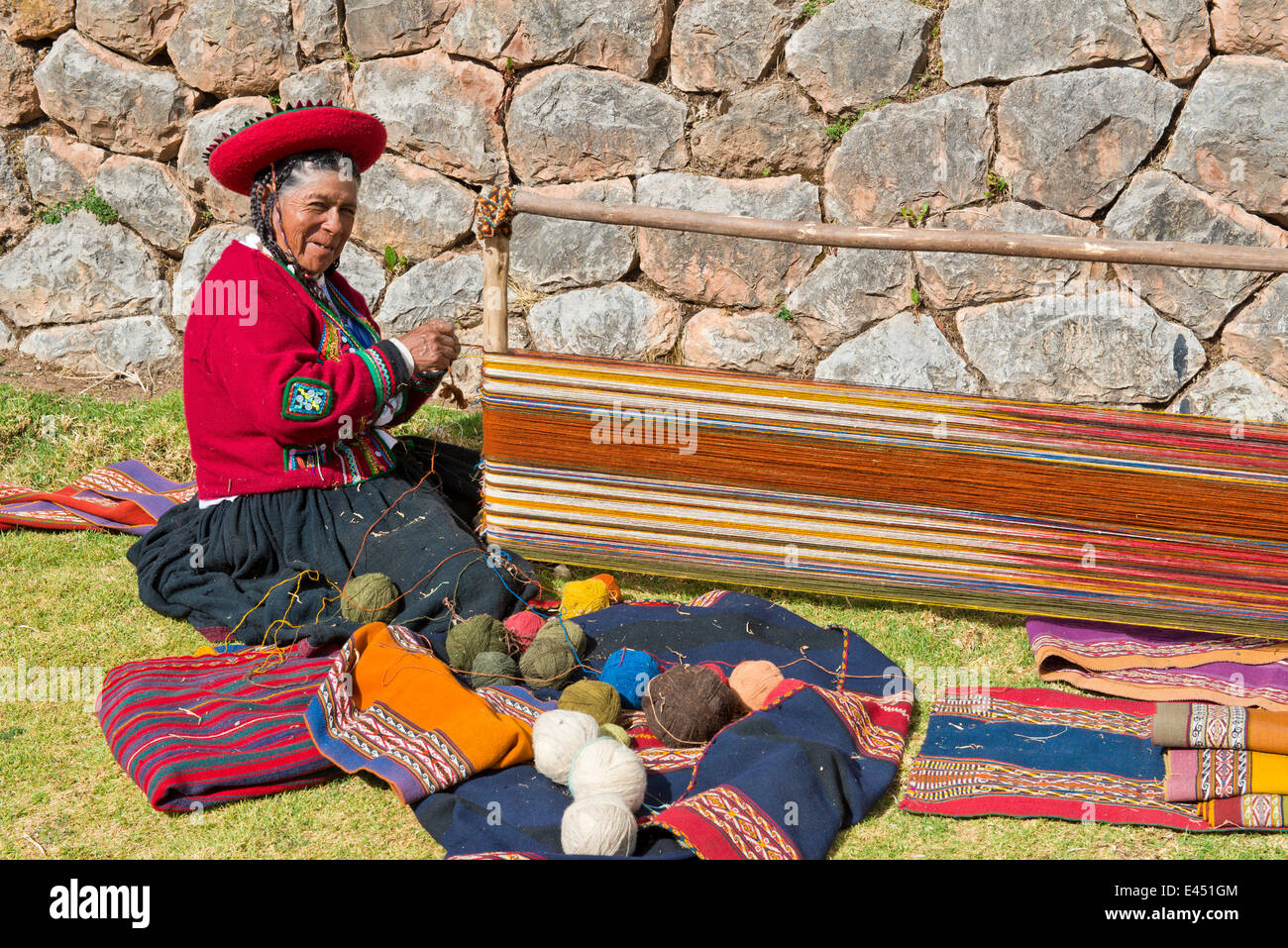 Donna anziana che indossa un cappello, Indiani Quechua in abito tradizionale seduta sul pavimento a lavorare sulla barella di un telaio di tessitura Foto Stock