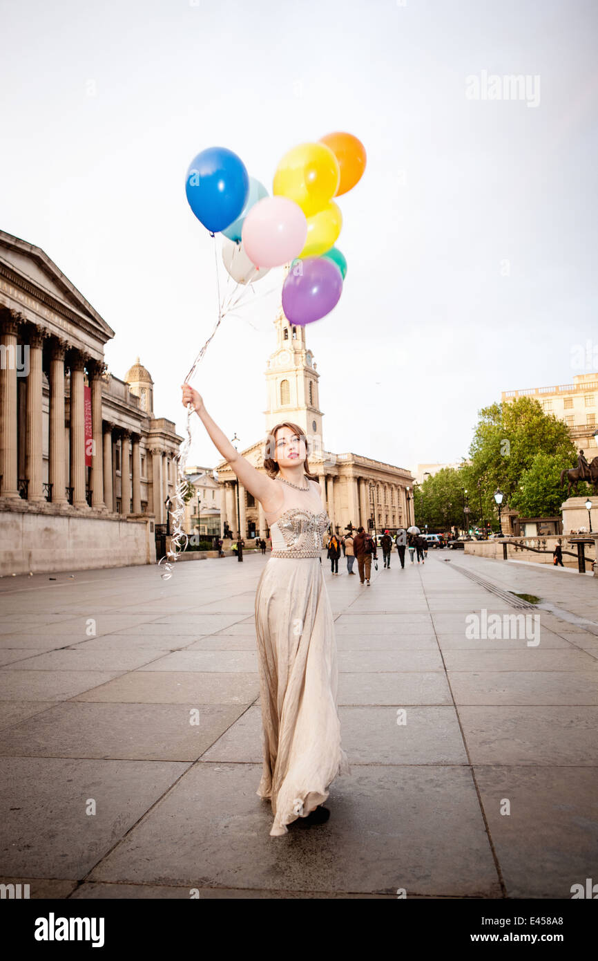 Giovane donna in abito da sera tenendo premuto fino palloncini, Trafalgar Square, London, Regno Unito Foto Stock