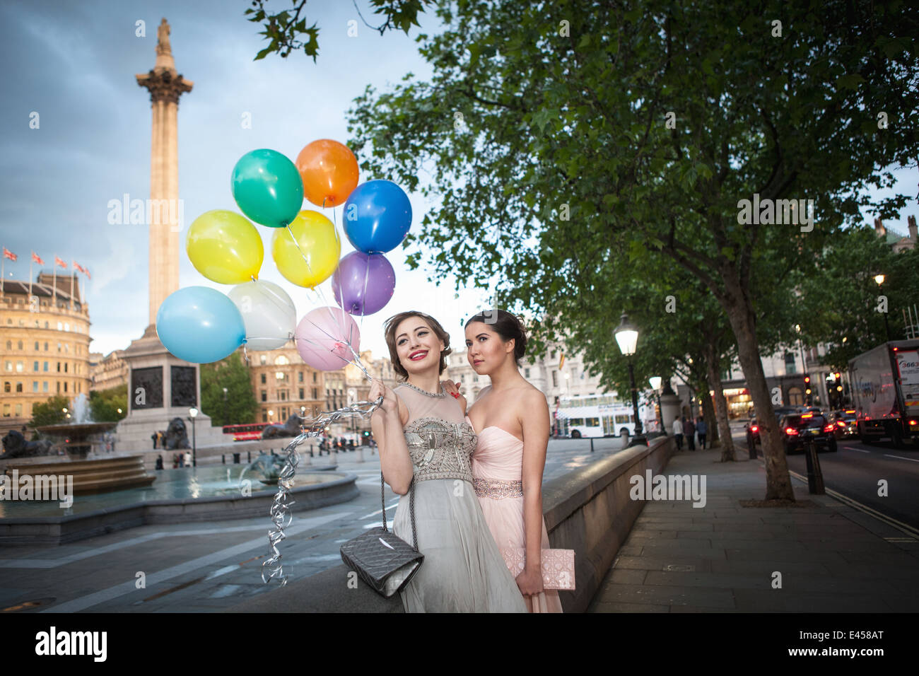 Due giovani amici di sesso femminile in sera abiti in posa con palloncini, Trafalgar Square, London, Regno Unito Foto Stock