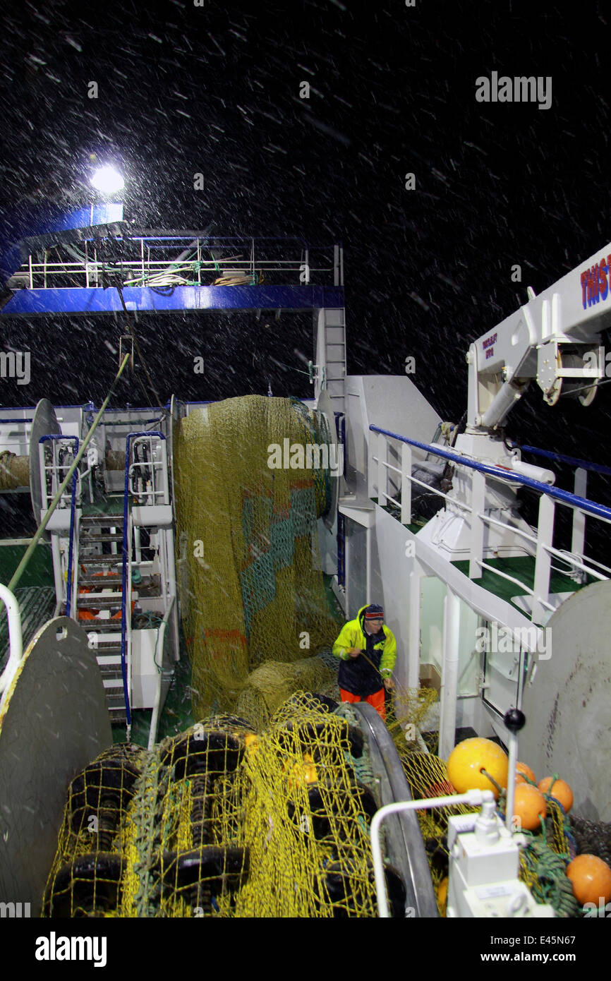 Trawlerman rammendo reti sulla nave da pesca con reti da traino della copertura durante una notte invernale sul mare del Nord, febbraio 2010. Modello di proprietà e rilasciato. Foto Stock