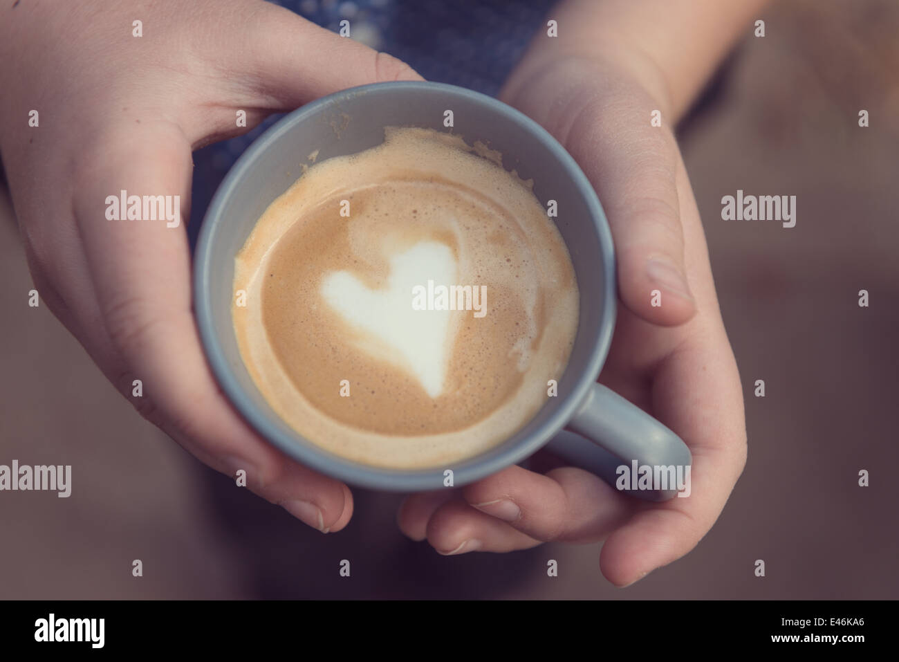 Mani tenendo una tazza di colore grigio con amore a forma di cuore in crema Foto Stock