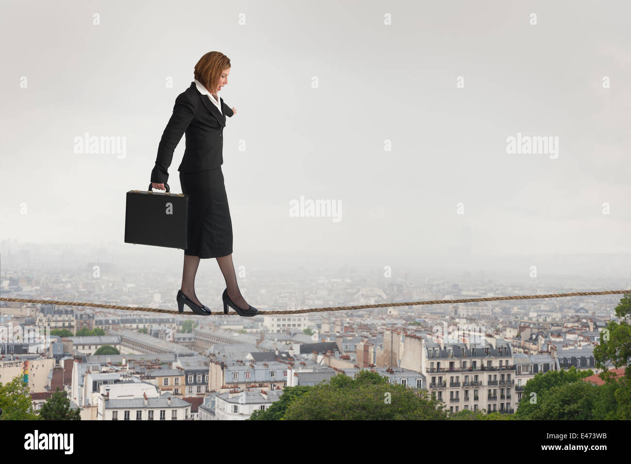 Imprenditrice a piedi una fune o bilanciamento highwire sopra i tetti della città Foto Stock