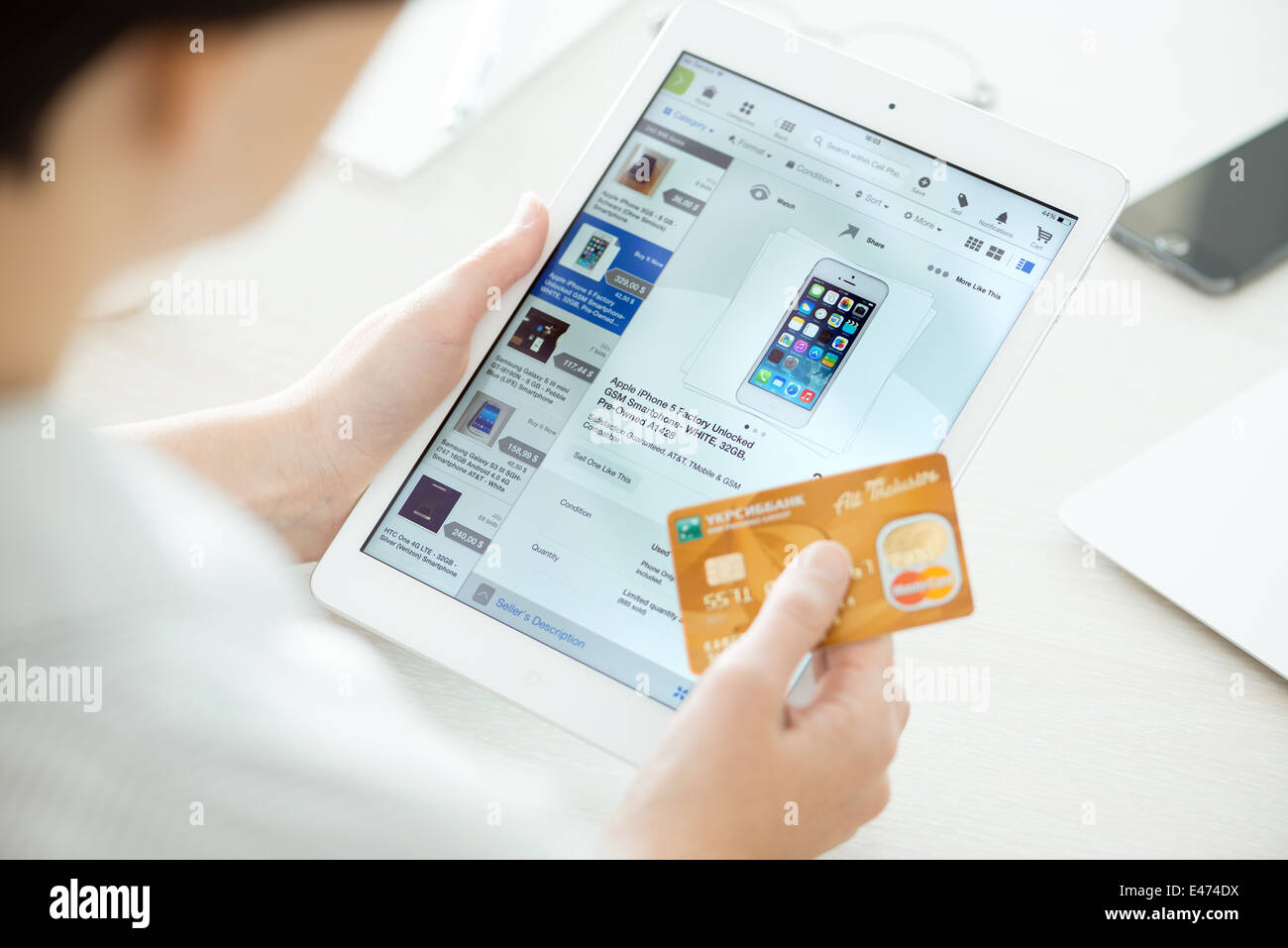Persona in possesso di una carta di credito e cercando di acquistare un nuovo Apple iPhone 5 con applicazione di eBay su un marchio nuovo Apple iPad aria Foto Stock