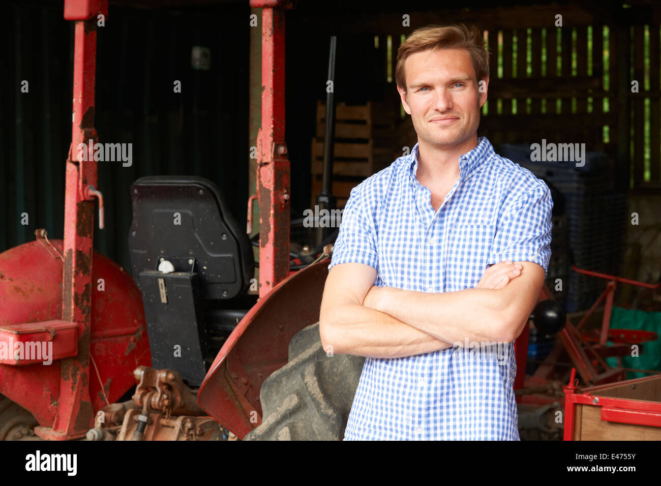 Agricoltore in piedi accanto al vecchio trattore nel fienile Foto Stock