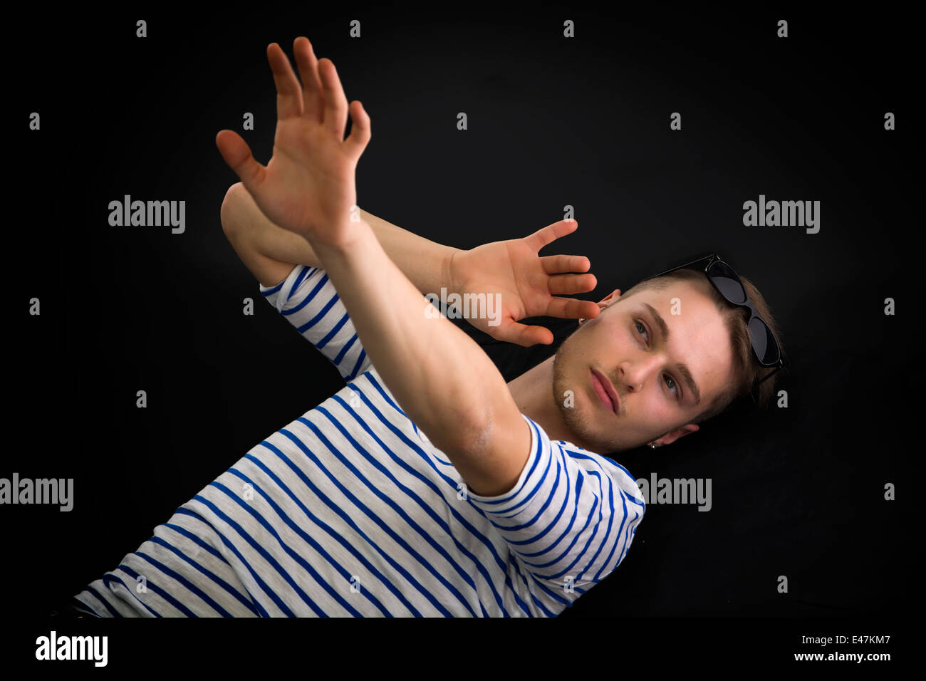 Giovane uomo posa sul pavimento nero proteggere se stesso con le mani, ripresa dall'alto Foto Stock