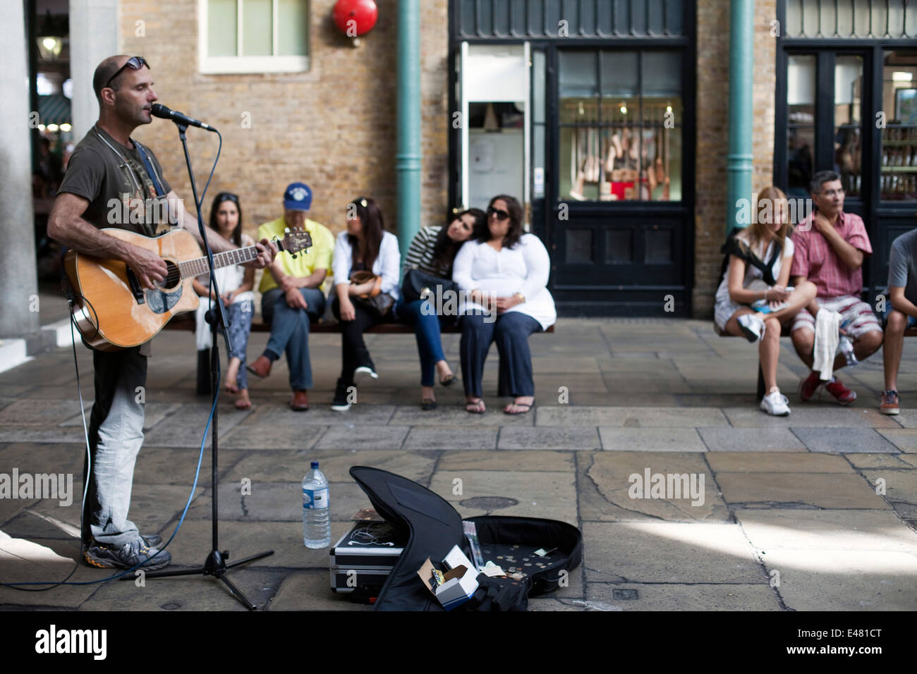 Un musicista canta e suona la chitarra per un pubblico nel mercato di Covent Garden Piazza. Londra, Regno Unito Foto Stock