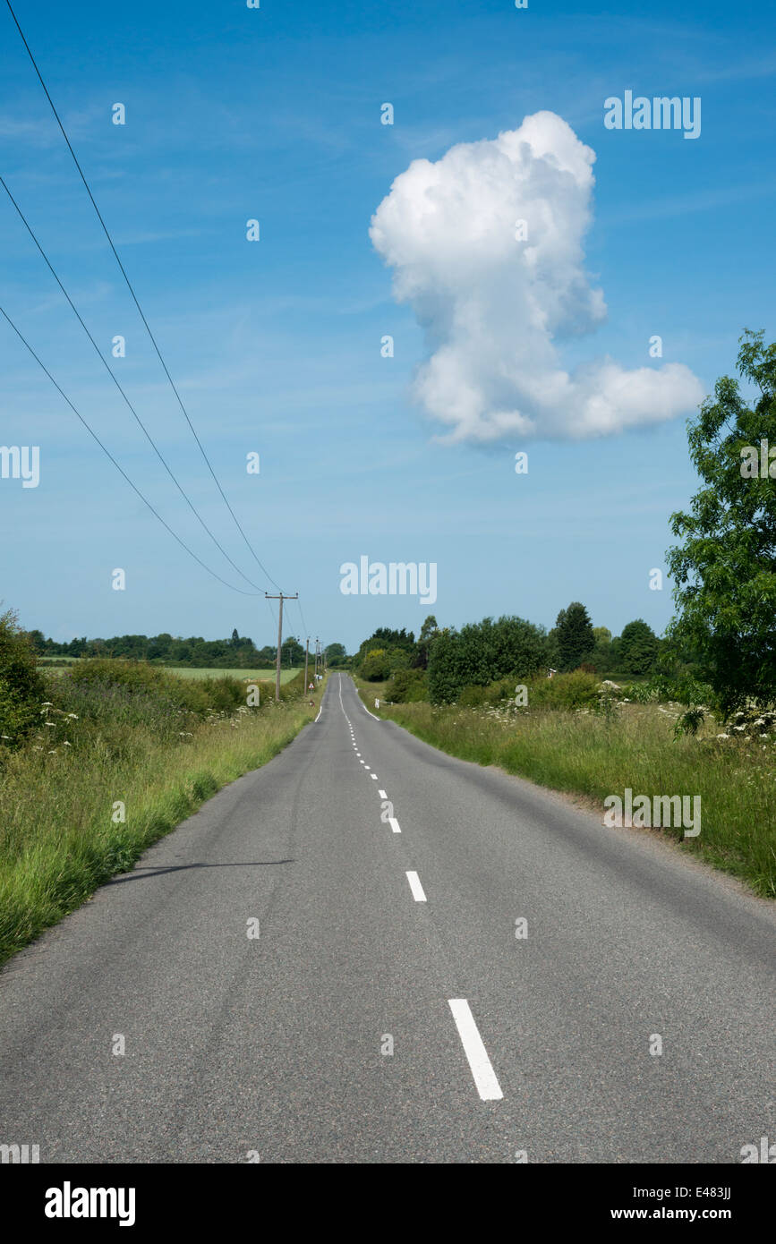 Una dritta strada di campagna nel Regno Unito, vuoto, che conduce a un punto di fuga con un cielo blu ed una nube bianca Foto Stock
