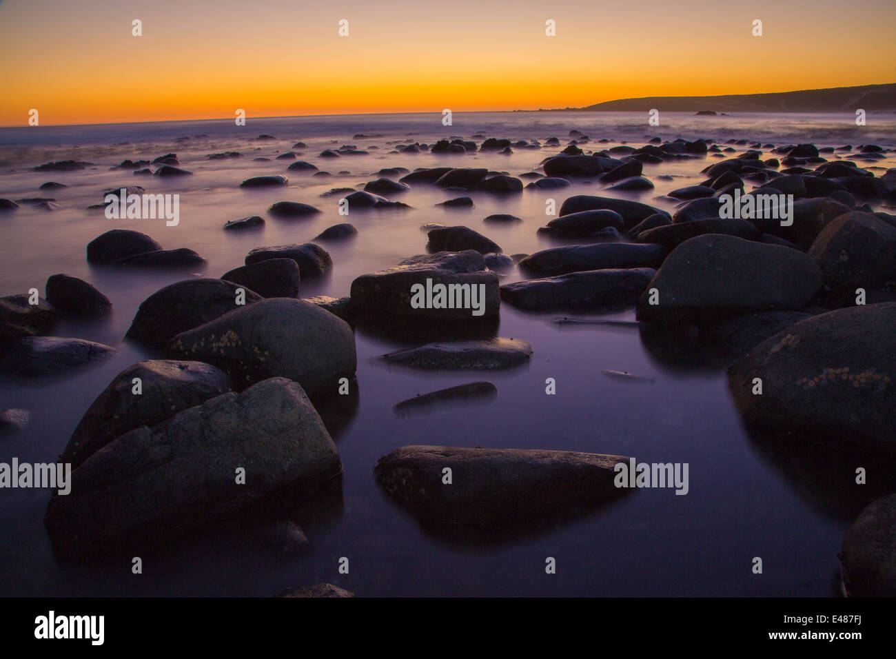 Round rocce nere nell'oceano con l'impostazione suns in background. Foto Stock