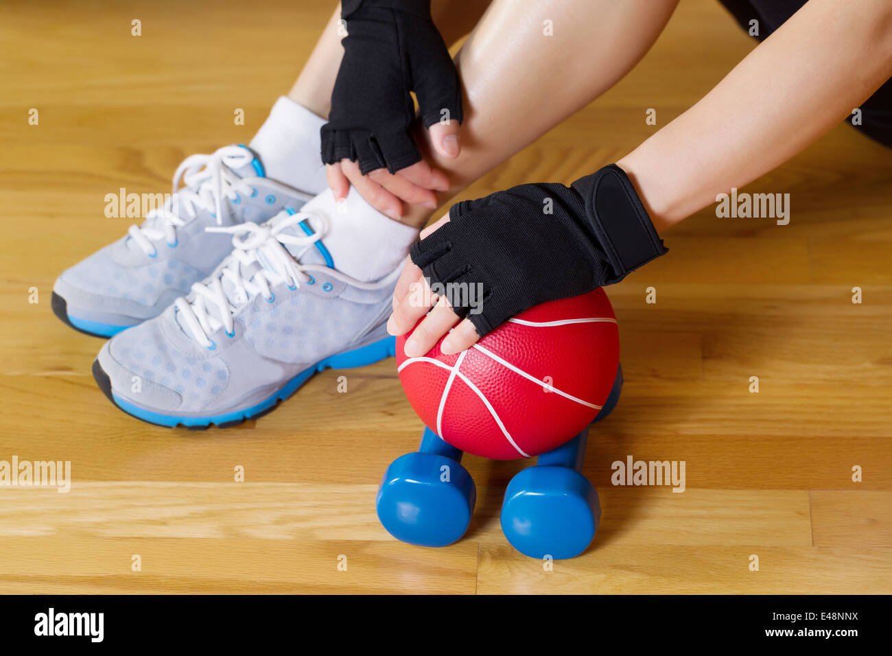 Immagine di mani femminili indossando guanti di allenamento mentre la mano appoggiata sul piccolo peso sfera con palestra in legno Piano e parziale del corpo Foto Stock