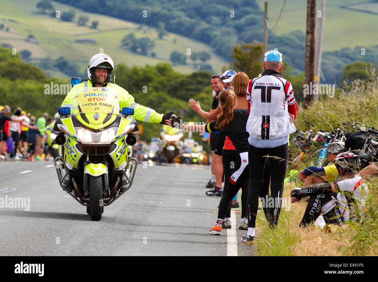 Addingham, nello Yorkshire, Regno Unito. 6 Luglio, 2014. Un sorridente polizia motociclista battendo il cinque in attesa di spettatori lungo il Tour de France route. Credito: Christina Bollen/Alamy Live News Foto Stock