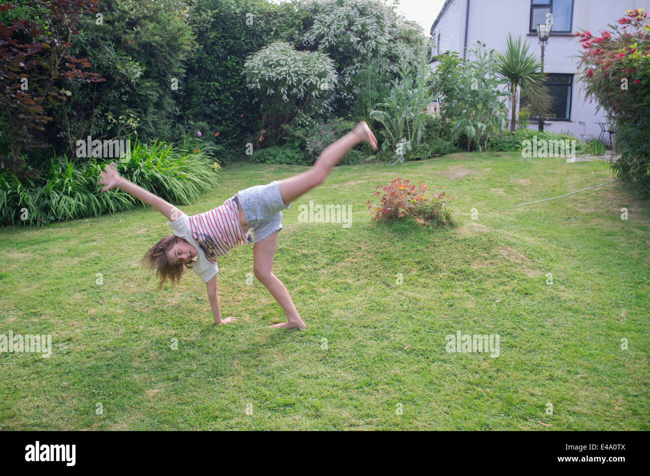 Un figlio di dieci anni di pratiche ragazza cartwheels in giardino Foto Stock