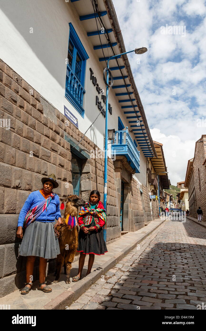 Le donne con il tradizionale abito lungo Tupac Yupanqui Palace Hotel parete su San Agustin street, Cuzco, UNESCO, Perù Foto Stock