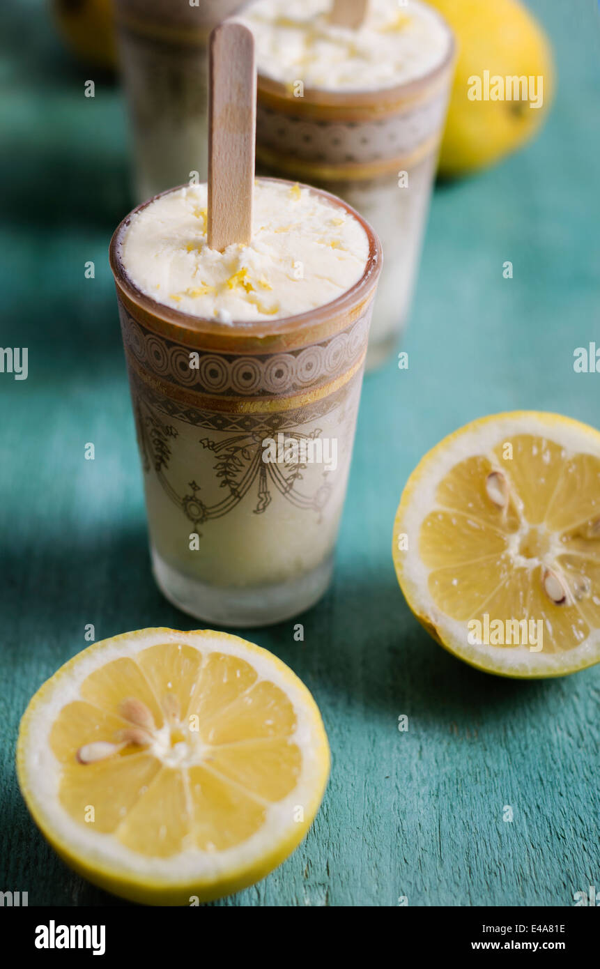 Bicchieri di fatti in casa a base di crema di limone Gelato e limoni a fettine su legno colorato Foto Stock
