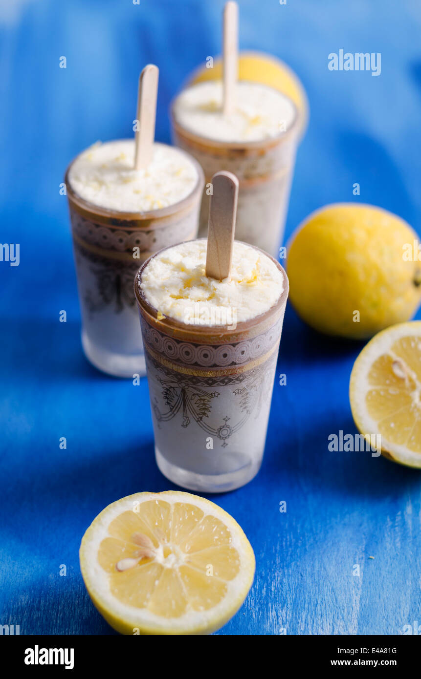 Bicchieri di fatti in casa a base di crema di limone Gelato e limoni a fettine su legno blu Foto Stock