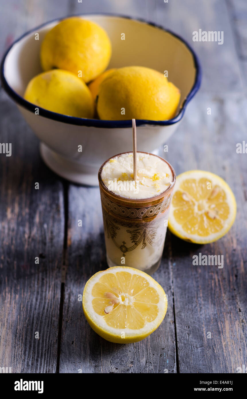 Ciotola di limoni, vetro di fatti in casa a base di crema di limone Gelato e fette di limone su legno Foto Stock