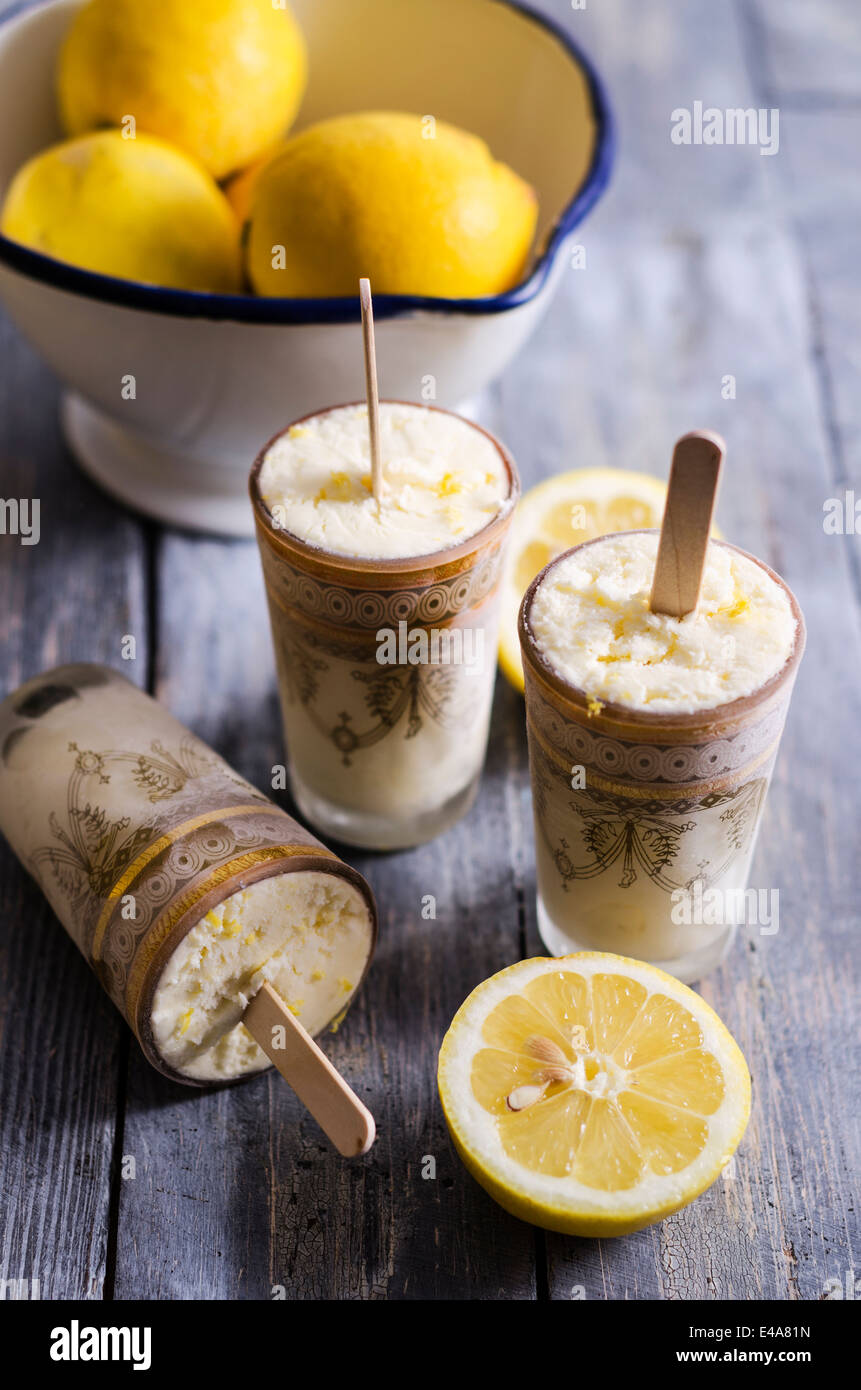 Ciotola di limoni, bicchieri di fatti in casa a base di crema di limone Gelato e fette di limone su legno Foto Stock